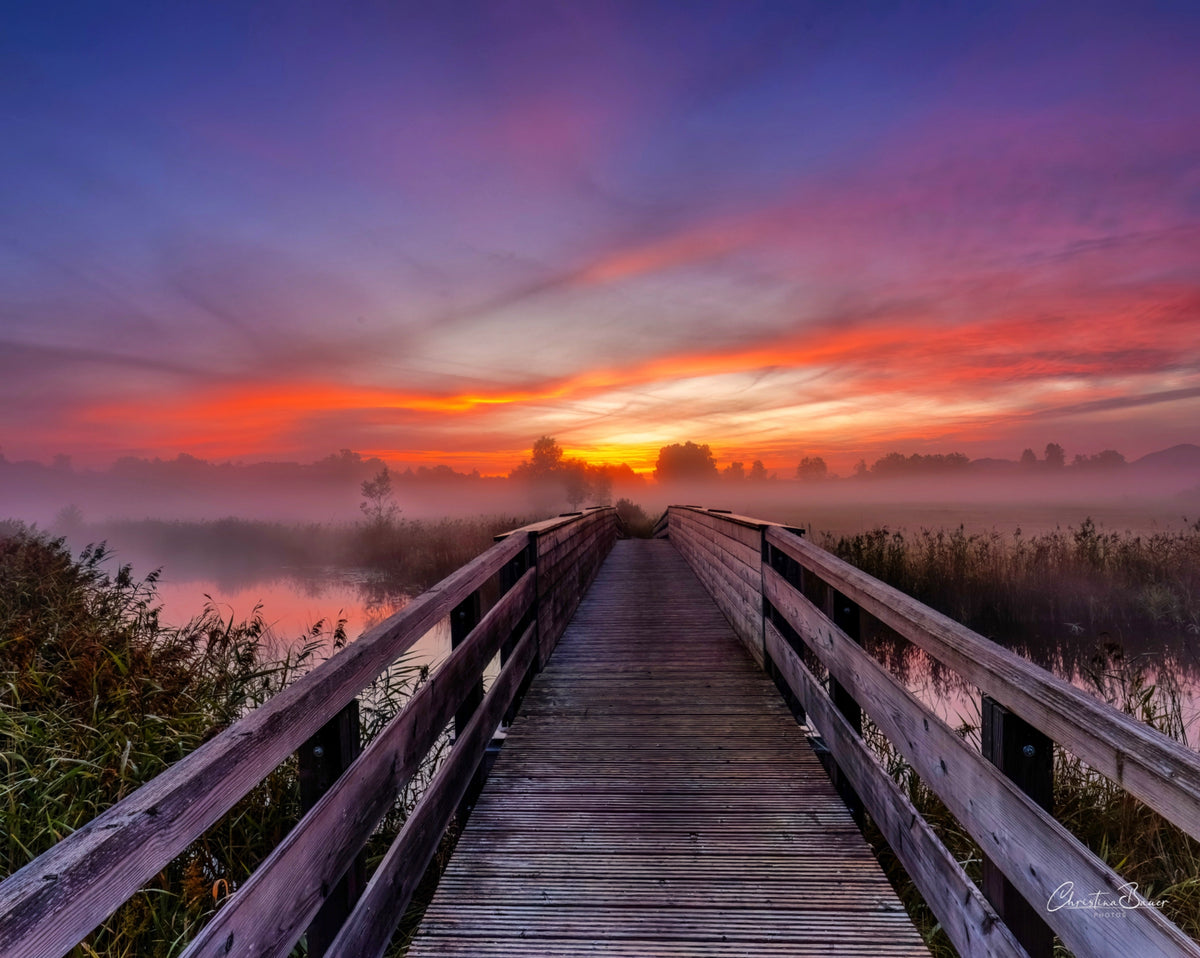 Holzsteg über stilles Wasser bei leuchtend rotem Abendhimmel und Nebel – Naturfotografie aus dem Blauen Land in Oberbayern