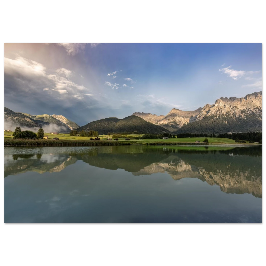 
Horizontales, ungerahmtes Poster mit Landschaftsmotiv: ruhiger Bergsee mit klarer Spiegelung, grüne Wiesen, kleine Hütten und das Karwendelgebirge im warmen Licht der goldenen Stunde unter einem dramatischen Himmel.
