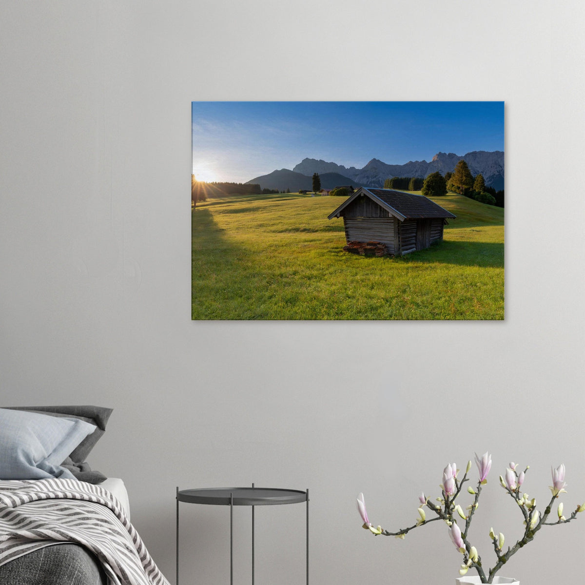 Leinwandbild mit traditioneller Holzhütte auf einer sonnigen, grünen Almwiese vor der beeindruckenden Bergkulisse des Karwendelgebirges. Warmes Morgenlicht taucht die idyllische Alpenlandschaft in eine natürliche, ruhige Stimmung.
