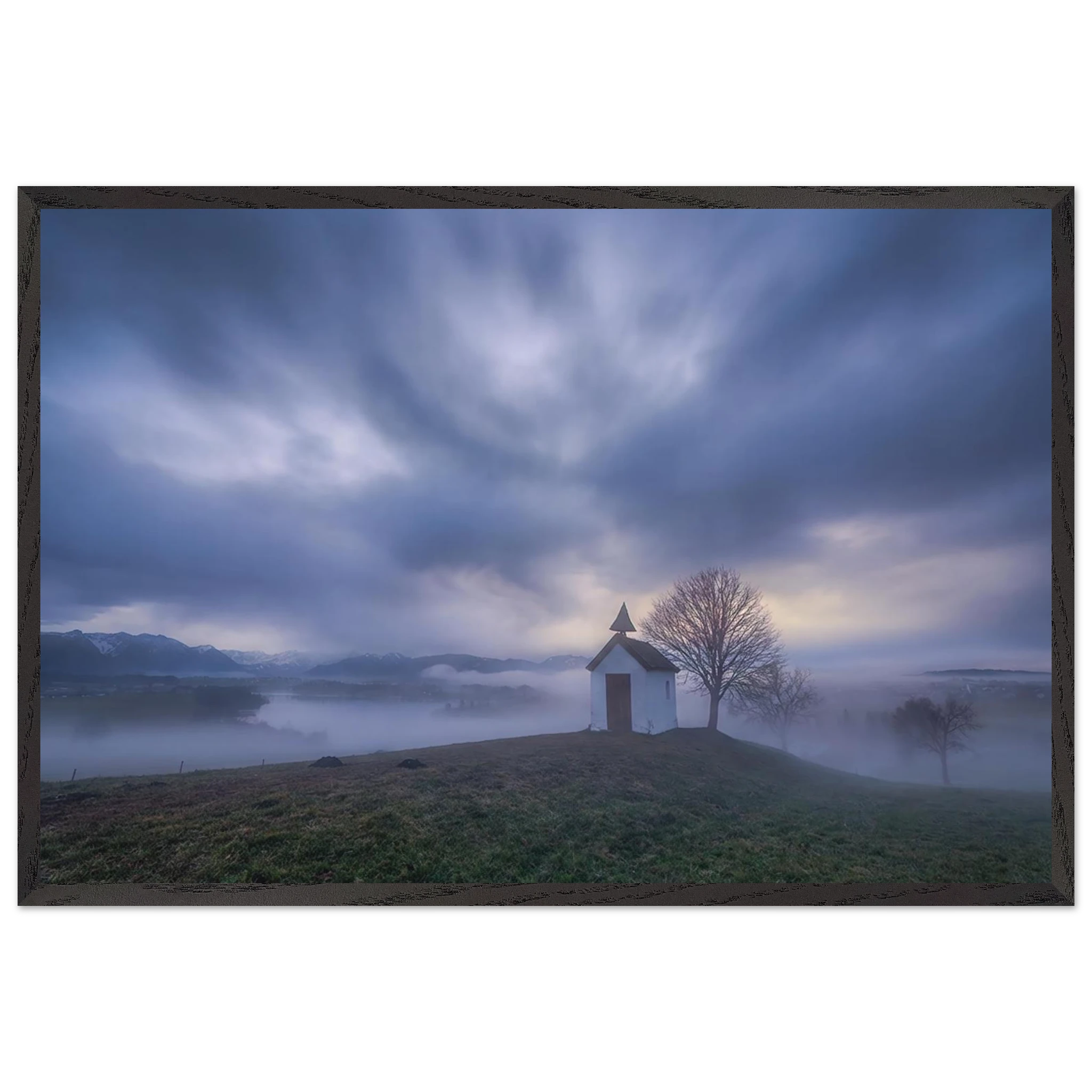 Hoch über der Landschaft bei Aidling im Blauen Land steht die kleine Mesnerhauskapelle – still, schlicht und eingebettet in einen Morgen, der kaum leiser sein könnte. Nebelschleier ziehen durch die Landschaft, während sich das erste Licht vorsichtig seinen Weg durch Wolken und Himmel bahnt. Die Weite öffnet den Blick, die Zeit scheint für einen Augenblick langsamer zu werden.

Die besondere Stimmung dieses Moments lebt vom Zusammenspiel aus weichem Licht, ziehenden Wolken und den sanften Konturen des Landes