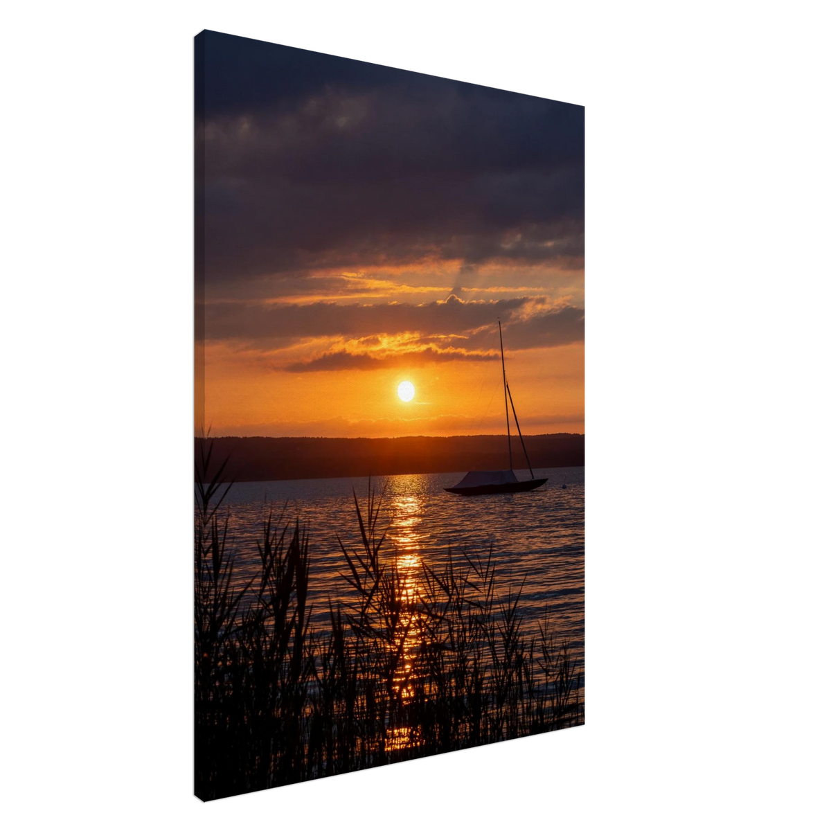 Vertikales Leinwandbild mit sommerlichem Sonnenuntergang am Ammersee in Bayern, golden leuchtender Sonne über dem Wasser, warmen orangefarbenen Wolken, Spiegelung auf dem See, Segelboot und dunklem Schilf im Vordergrund.