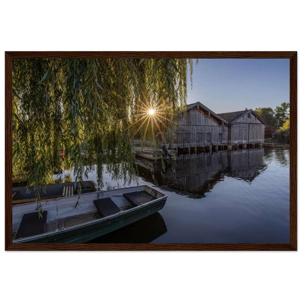Gerahmtes Premium-Matt-Poster mit Bootshäusern in Seehausen am Staffelsee bei warmer Morgensonne, eingefasst in einen dunkelbraunen Holzrahmen.