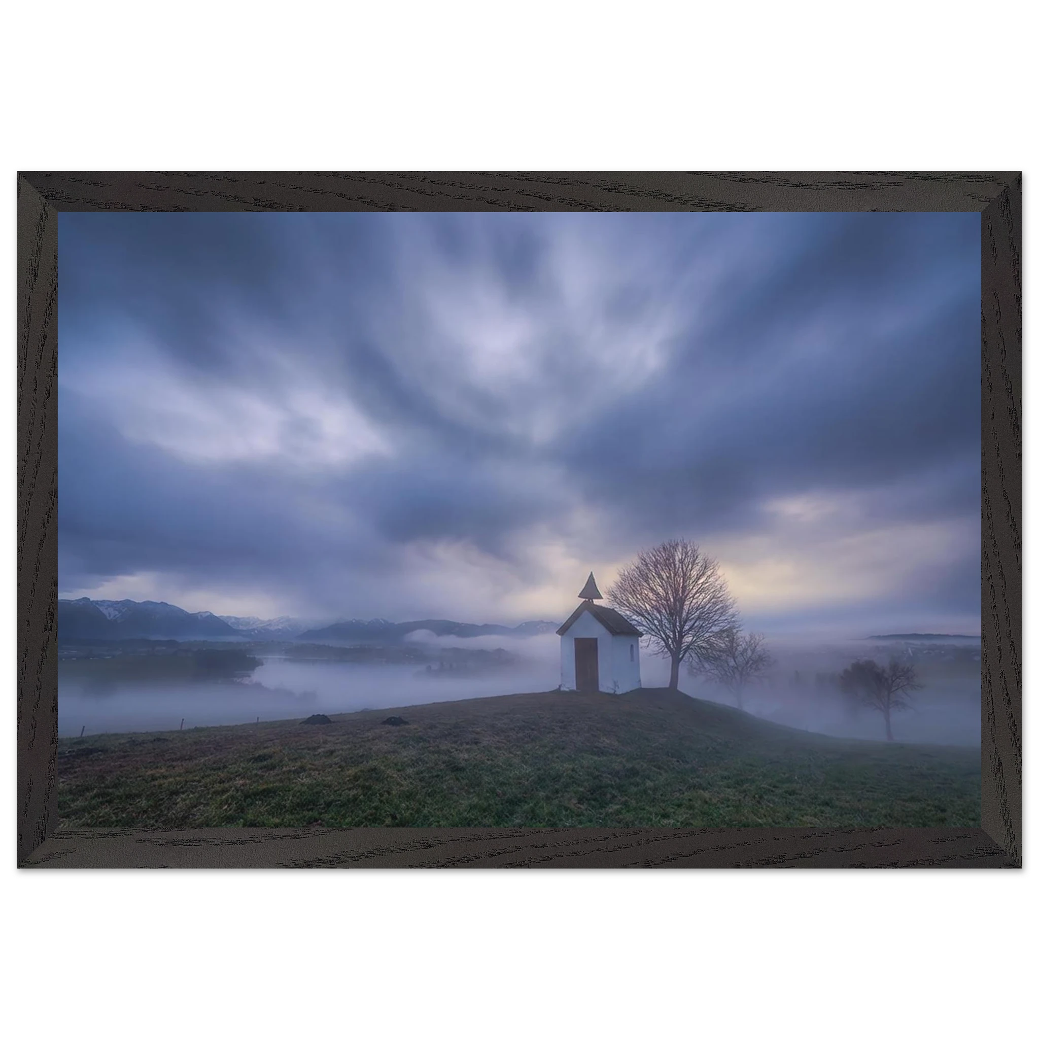 Hoch über der Landschaft bei Aidling im Blauen Land steht die kleine Mesnerhauskapelle – still, schlicht und eingebettet in einen Morgen, der kaum leiser sein könnte. Nebelschleier ziehen durch die Landschaft, während sich das erste Licht vorsichtig seinen Weg durch Wolken und Himmel bahnt. Die Weite öffnet den Blick, die Zeit scheint für einen Augenblick langsamer zu werden.

