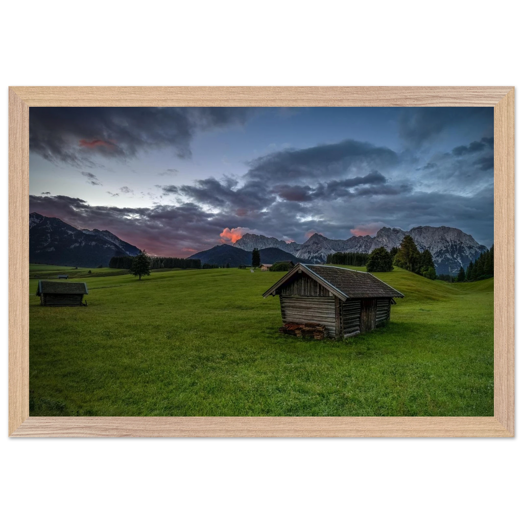 Grüne Buckelwiesen bei Krün mit traditionellen Heustadeln, dem Karwendelgebirge im Hintergrund und dramatischen Regenwolken in der frühen Morgenstimmung.
