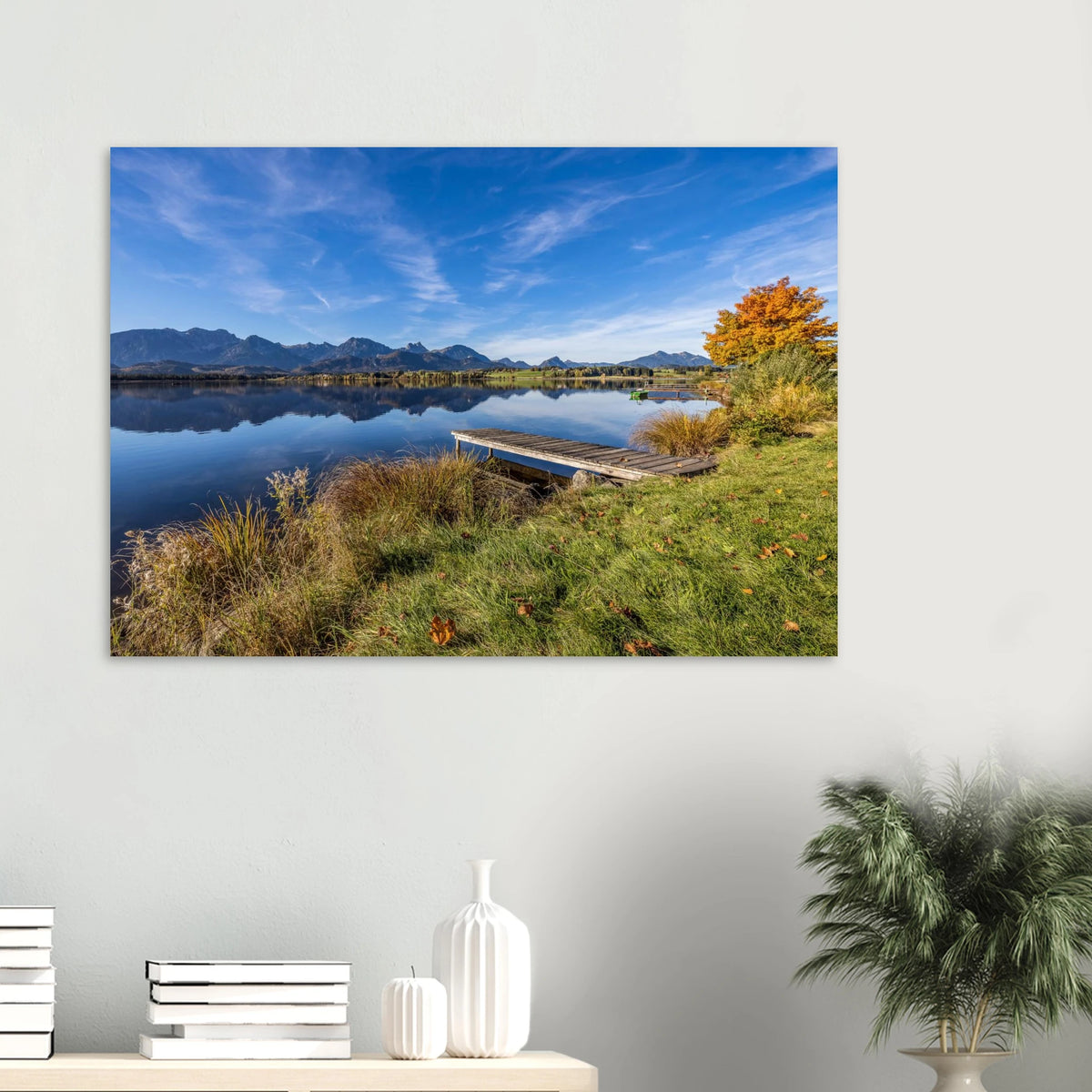 Herbstlicher Hopfensee mit ruhigem, spiegelndem Wasser, Holzsteg und leuchtend goldenem Baum vor der klaren Kulisse der Allgäuer Alpen.
