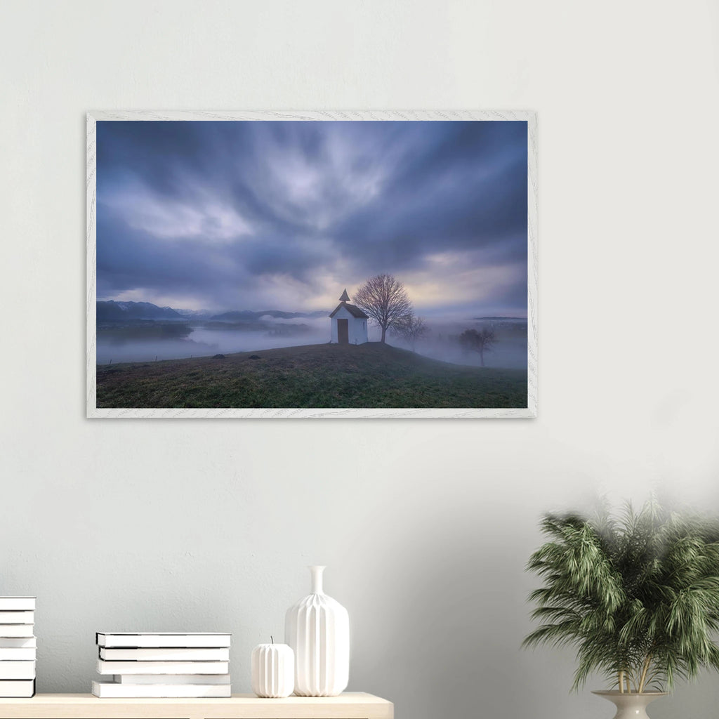 Hoch über der Landschaft bei Aidling im Blauen Land steht die kleine Mesnerhauskapelle – still, schlicht und eingebettet in einen Morgen, der kaum leiser sein könnte. Nebelschleier ziehen durch die Landschaft, während sich das erste Licht vorsichtig seinen Weg durch Wolken und Himmel bahnt. Die Weite öffnet den Blick, die Zeit scheint für einen Augenblick langsamer zu werden.

Die besondere Stimmung dieses Moments lebt vom Zusammenspiel aus weichem Licht, ziehenden Wolken und den sanften Konturen des Landes
