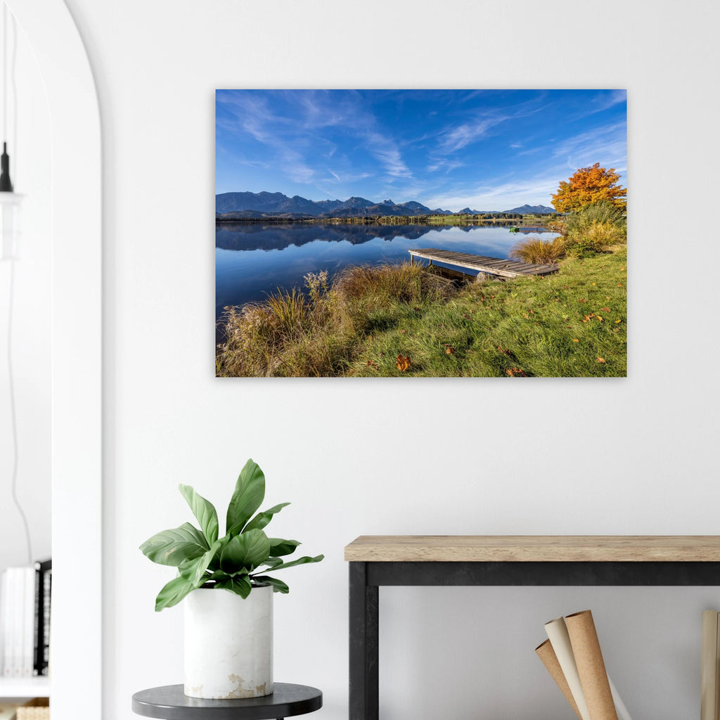 Herbstlicher Hopfensee mit ruhigem, spiegelndem Wasser, Holzsteg und leuchtend goldenem Baum vor der klaren Kulisse der Allgäuer Alpen.
