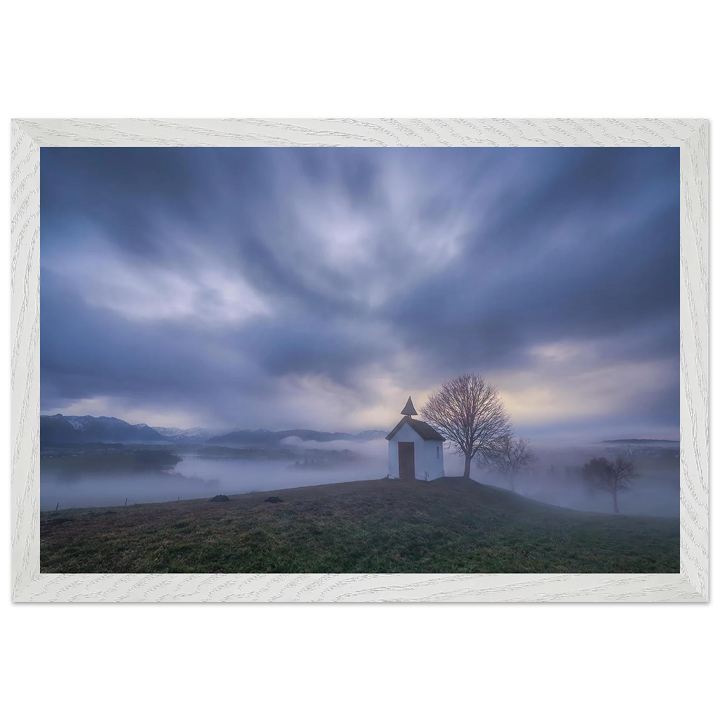 Hoch über der Landschaft bei Aidling im Blauen Land steht die kleine Mesnerhauskapelle – still, schlicht und eingebettet in einen Morgen, der kaum leiser sein könnte. Nebelschleier ziehen durch die Landschaft, während sich das erste Licht vorsichtig seinen Weg durch Wolken und Himmel bahnt. Die Weite öffnet den Blick, die Zeit scheint für einen Augenblick langsamer zu werden.

Die besondere Stimmung dieses Moments lebt vom Zusammenspiel aus weichem Licht, ziehenden Wolken und den sanften Konturen des Landes