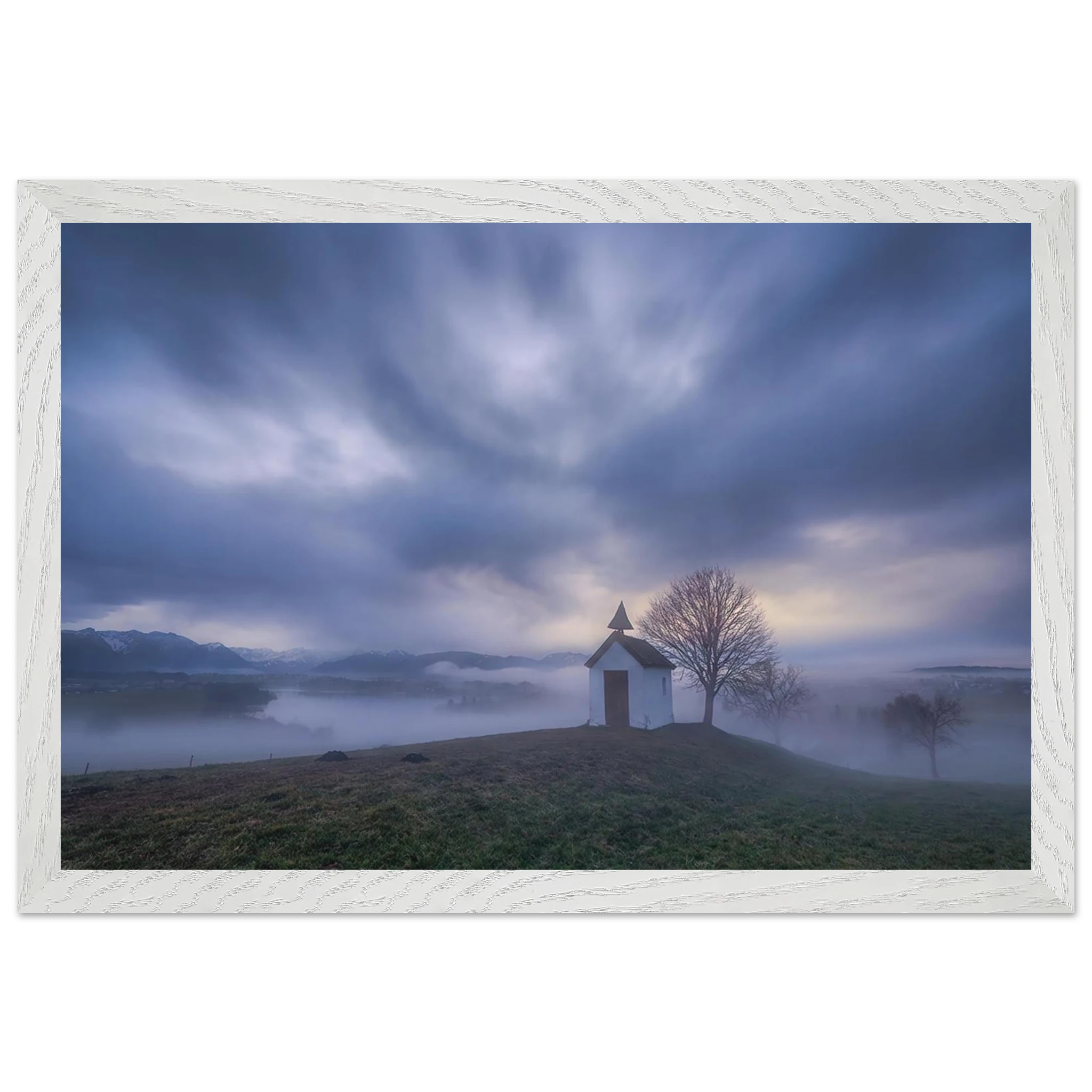 Hoch über der Landschaft bei Aidling im Blauen Land steht die kleine Mesnerhauskapelle – still, schlicht und eingebettet in einen Morgen, der kaum leiser sein könnte. Nebelschleier ziehen durch die Landschaft, während sich das erste Licht vorsichtig seinen Weg durch Wolken und Himmel bahnt. Die Weite öffnet den Blick, die Zeit scheint für einen Augenblick langsamer zu werden.

Die besondere Stimmung dieses Moments lebt vom Zusammenspiel aus weichem Licht, ziehenden Wolken und den sanften Konturen des Landes