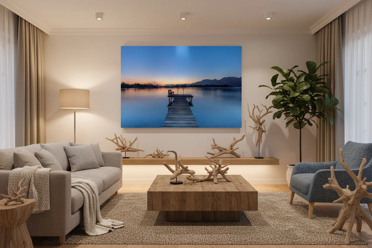 Aluminium-Print mit Sonnenaufgang am Kochelsee: Ruhiger See in sanften Blau- und Orangetönen, ein hölzerner Steg mit Bank führt ins stille Wasser, im Hintergrund Berge und die zarte Morgenstimmung des beginnenden Tages.