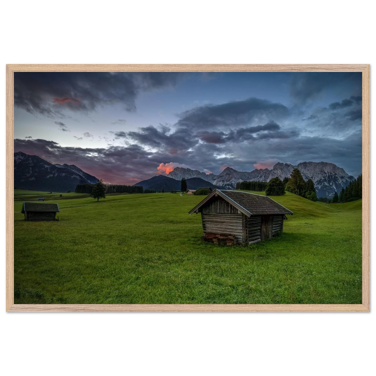Grüne Buckelwiesen bei Krün mit traditionellen Heustadeln, dem Karwendelgebirge im Hintergrund und dramatischen Regenwolken in der frühen Morgenstimmung.
