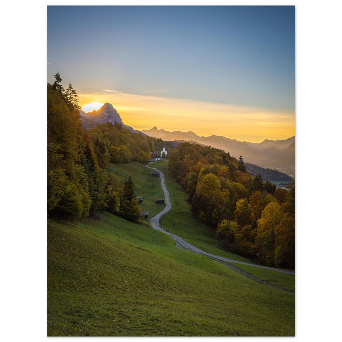 Vertikales Landschaftsposter mit einem stimmungsvollen Sonnenuntergang im Werdenfelserland. Ein geschwungener Weg führt durch Wiesen und herbstlich gefärbte Wälder hinauf nach Wamberg, dem höchstgelegenen Kirchdorf Deutschlands. Die kleine Kirche liegt eingebettet in die Berglandschaft, während die untergehende Sonne den Himmel in warme Gold- und Orangetöne taucht.