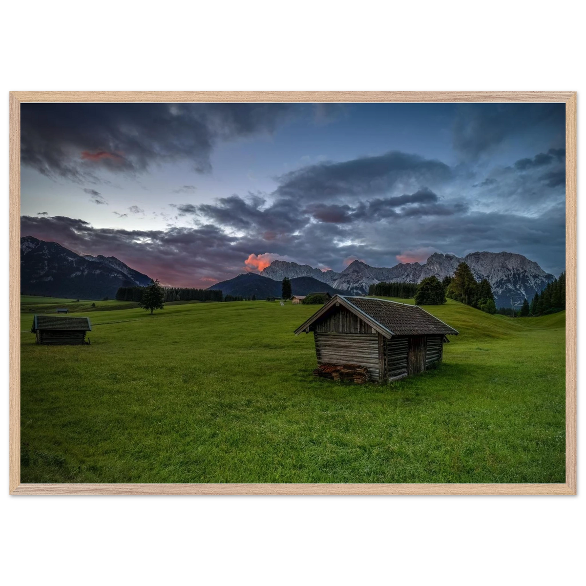 Grüne Buckelwiesen bei Krün mit traditionellen Heustadeln, dem Karwendelgebirge im Hintergrund und dramatischen Regenwolken in der frühen Morgenstimmung.
