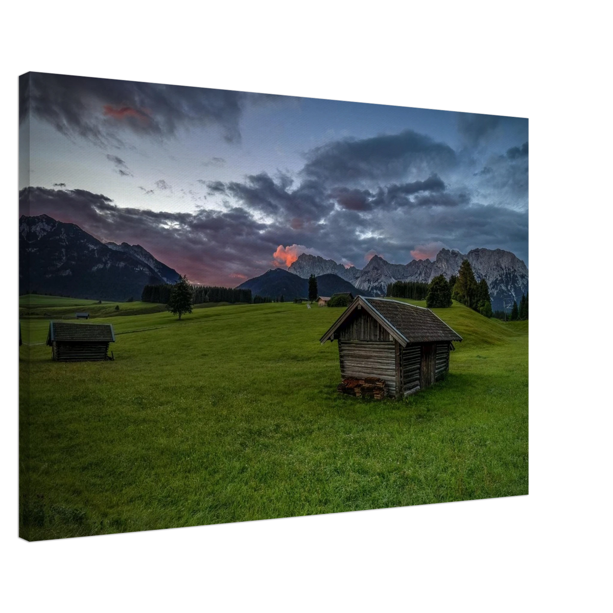 Grüne Buckelwiesen bei Krün mit traditionellen Heustadeln, dem Karwendelgebirge im Hintergrund und dramatischen Regenwolken in der frühen Morgenstimmung.
