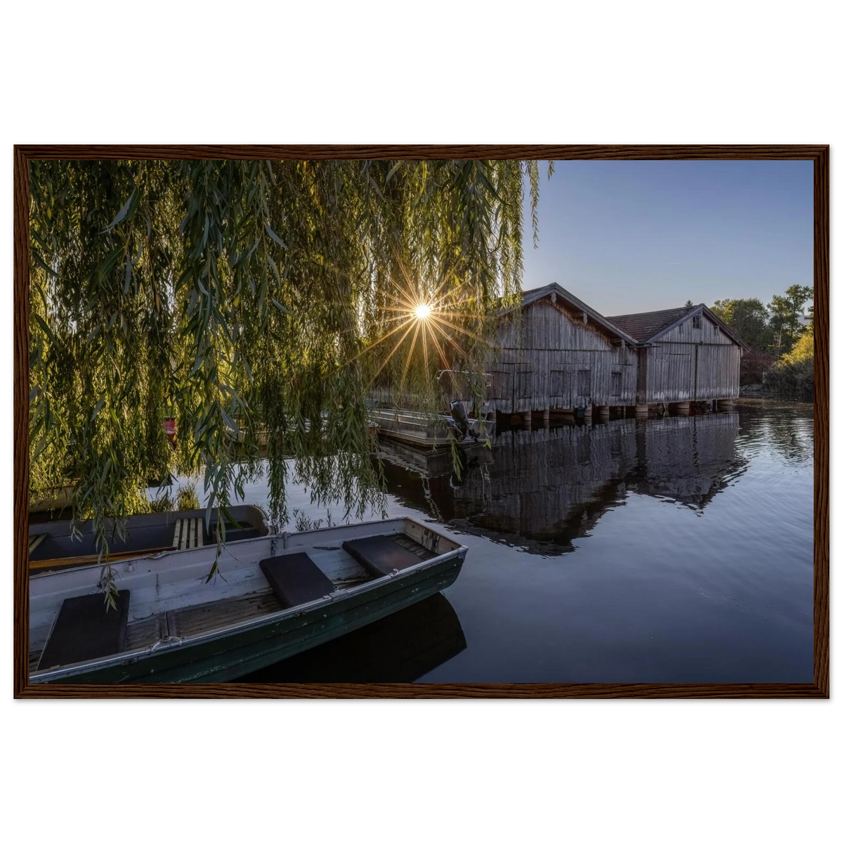 Gerahmtes Premium-Matt-Poster mit Bootshäusern in Seehausen am Staffelsee bei warmer Morgensonne, eingefasst in einen dunkelbraunen Holzrahmen.