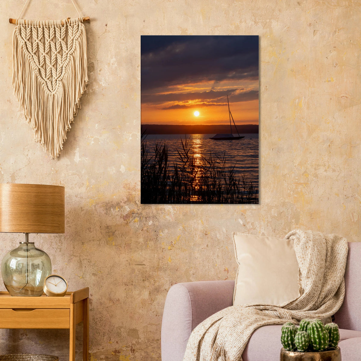 Vertikales Leinwandbild mit einem leuchtenden Sommer-Sonnenuntergang am Ammersee in Bayern. Goldene und orangefarbene Lichtstimmungen spiegeln sich auf dem Wasser, während ein Segelboot ruhig auf dem See liegt und feines Schilf im Vordergrund die natürliche Atmosphäre abrundet.