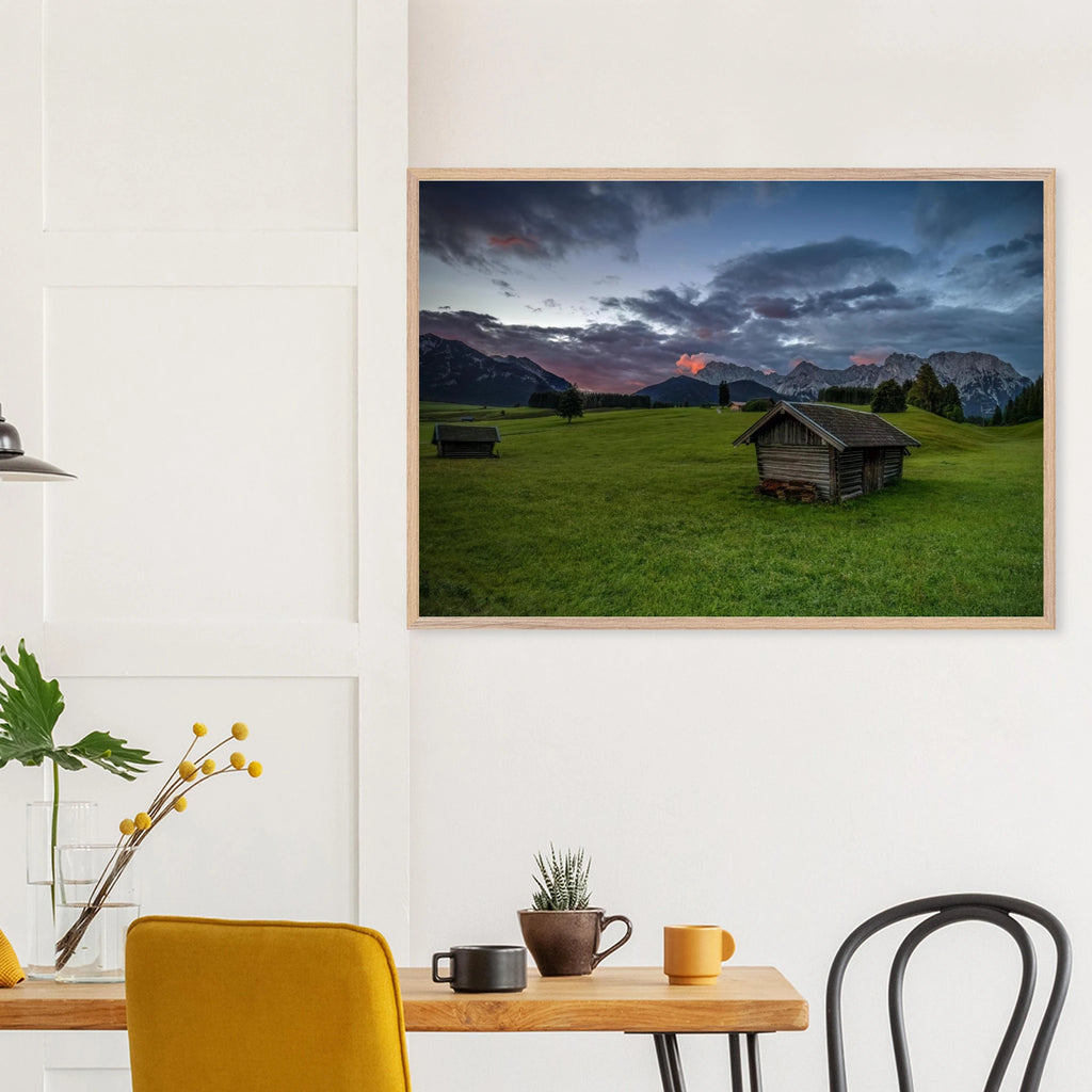 Grüne Buckelwiesen bei Krün mit traditionellen Heustadeln, dem Karwendelgebirge im Hintergrund und dramatischen Regenwolken in der frühen Morgenstimmung.
