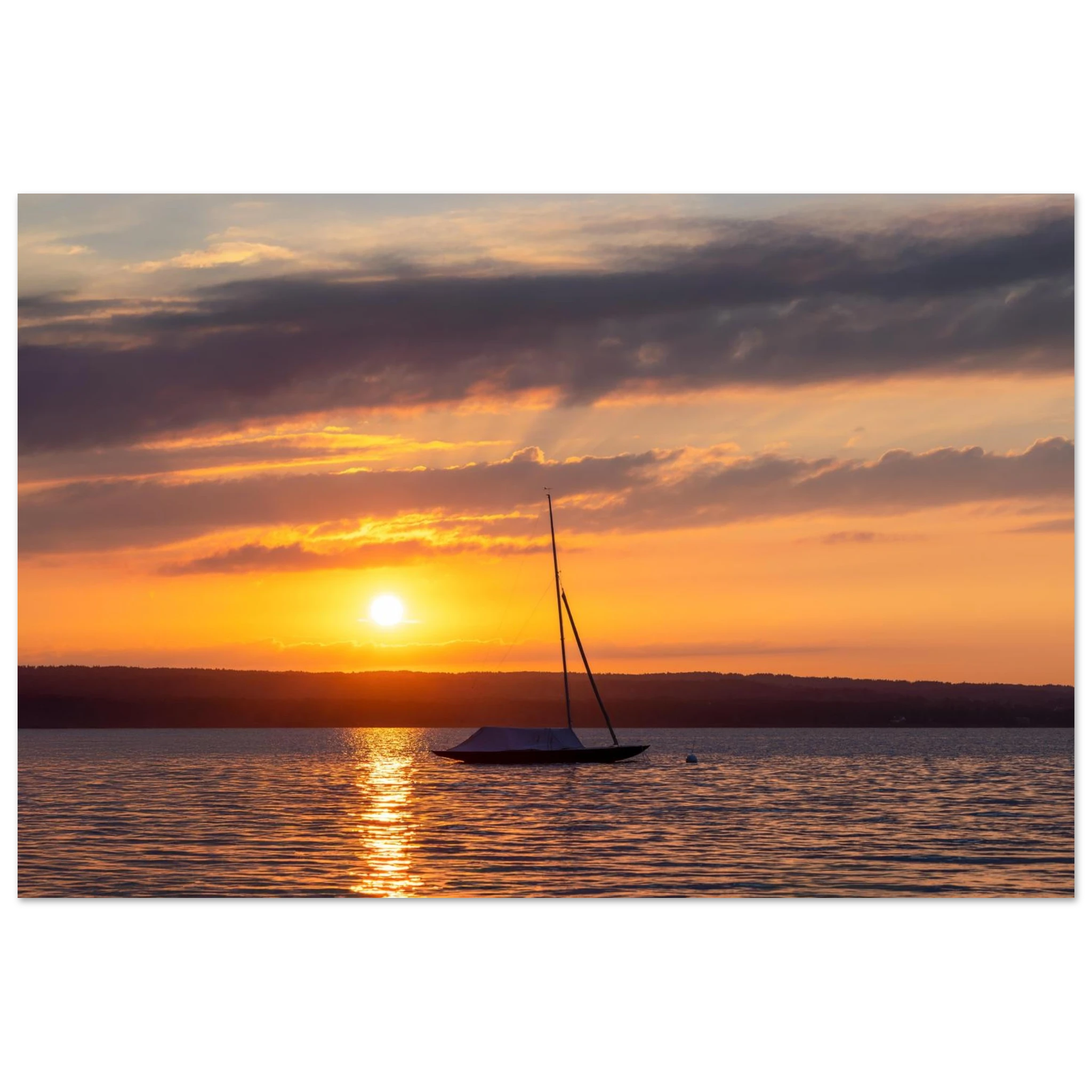 Premium Matt Poster „Ammersee Sonnenuntergang“ von Christina Bauer Photos. Ein einzelnes Segelboot liegt ruhig auf dem Wasser des Ammersees, während die untergehende Sonne den Himmel in warme Orange-, Gold- und sanfte Violetttöne taucht. Das Licht spiegelt sich auf der Wasseroberfläche und schafft eine ruhige, stimmungsvolle Atmosphäre voller Weite, Sommergefühl und natürlicher Eleganz.
