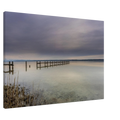 Leinwandbild mit ruhiger Ammersee-Landschaft in sanften Grau-, Beige- und Blautönen. Ein langer Holzsteg führt hinaus auf das spiegelglatte Wasser, während sich der weite Himmel mit seinen zarten Wolkenschichten im See widerspiegelt. Im Vordergrund sind Schilf und der klare, steinige Uferbereich sichtbar. Die hochwertige Leinwand auf 2 cm Keilrahmen bringt die feinen Farbverläufe und die stille Atmosphäre dieses zeitlosen Naturmotivs besonders harmonisch zur Geltung.