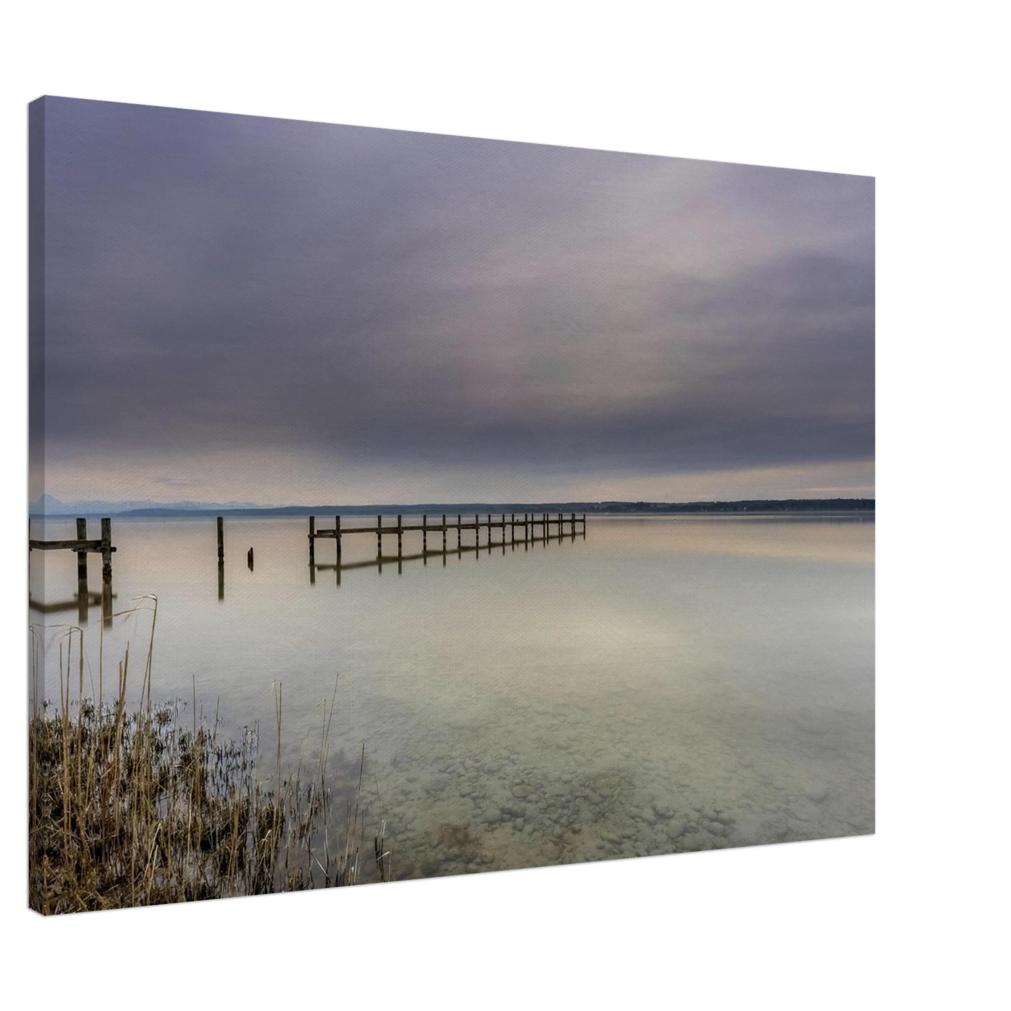 Leinwandbild mit ruhiger Ammersee-Landschaft in sanften Grau-, Beige- und Blautönen. Ein langer Holzsteg führt hinaus auf das spiegelglatte Wasser, während sich der weite Himmel mit seinen zarten Wolkenschichten im See widerspiegelt. Im Vordergrund sind Schilf und der klare, steinige Uferbereich sichtbar. Die hochwertige Leinwand auf 2 cm Keilrahmen bringt die feinen Farbverläufe und die stille Atmosphäre dieses zeitlosen Naturmotivs besonders harmonisch zur Geltung.