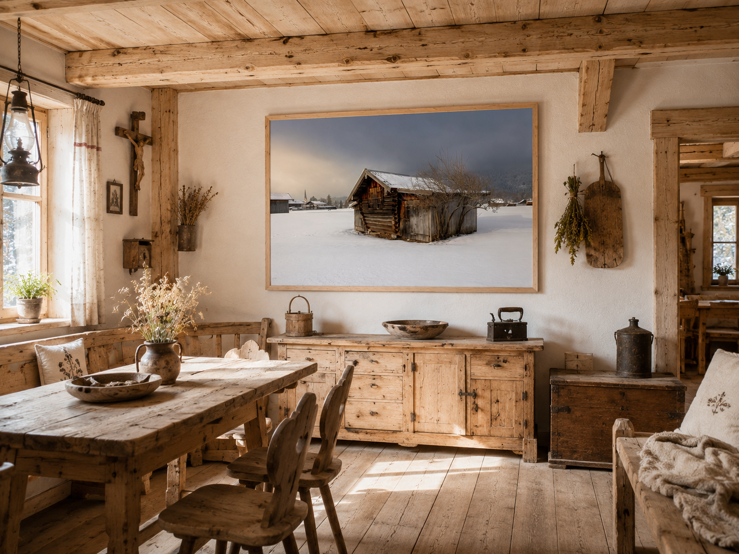 Helle, gemütliche Bauernstube mit alten naturbelassenen Holzbalken, rustikalem Esstisch und traditionellen Bauernmöbeln aus hellem Massivholz. Historische Dekorationen wie Holztruhen, alte Küchenutensilien, Trockenblumen und religiöse Wanddekoration verleihen dem Raum einen authentischen alpenländischen Charakter. An der hellen Wand hängt ein großes Poster im Format 70 × 100 cm mit naturfarbenem Holzrahmen. Das Motiv zeigt eine alte Holzhütte in einer verschneiten Winterlandschaft unter einem dramatischen W