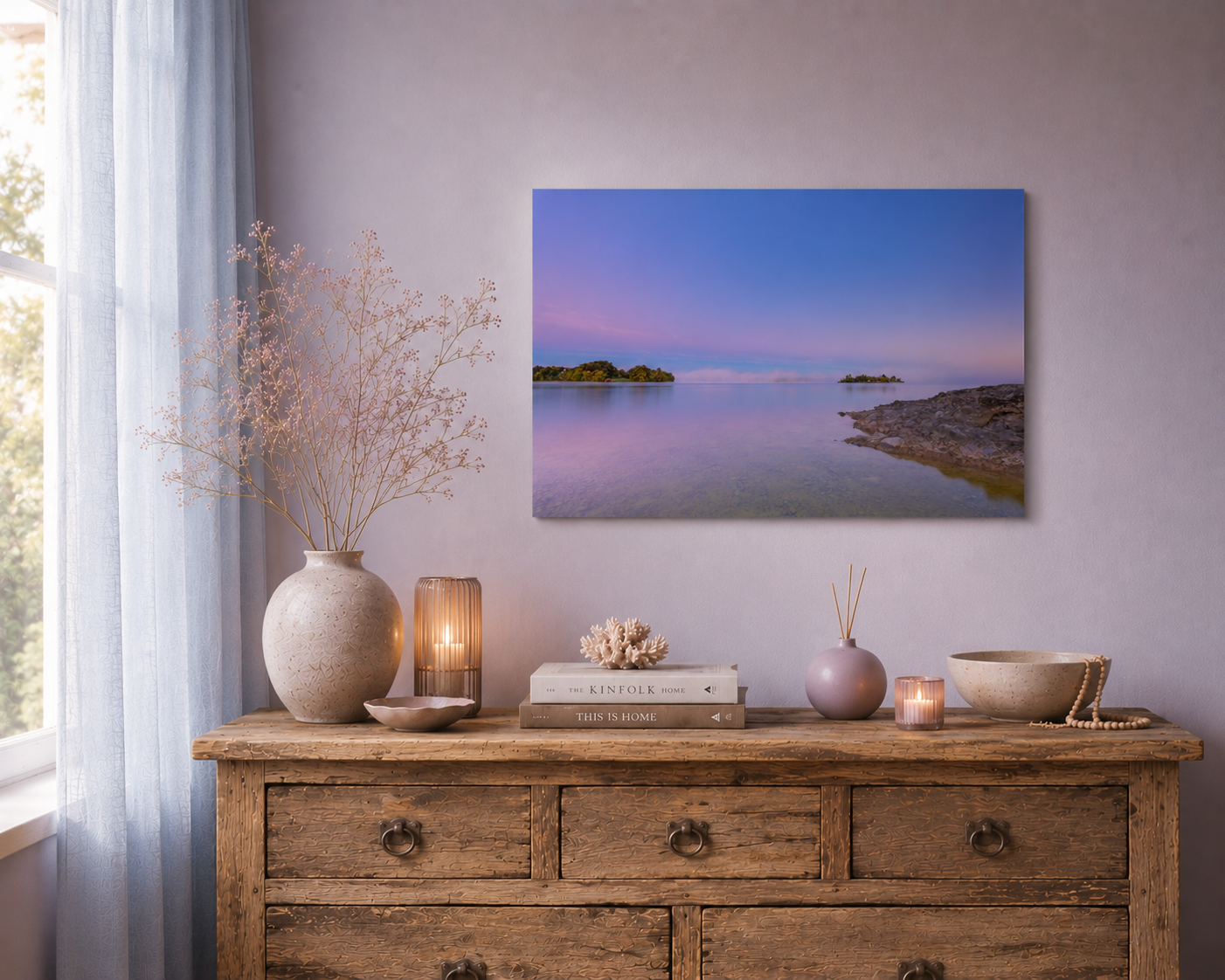 Aluminiumprint vom Staffelsee in sanften Blau- und Rosétönen über einer rustikalen Kommode aus altem Naturholz, kombiniert mit zarter pastellfarbener Dekoration, Kerzenlicht und hellblauen Vorhängen in einer ruhigen, harmonischen Wohnatmosphäre.