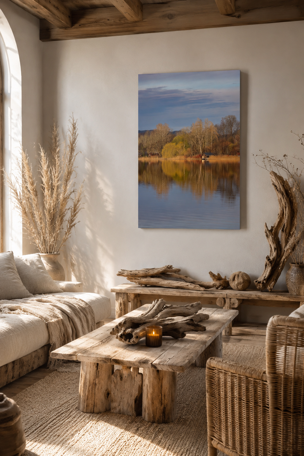 Naturbelassenes Wohnzimmer mit rustikalen Möbeln aus hellem Altholz und Treibholzdekoration. An der hellen Wand hängt ein vertikales Leinwandbild im Format 60x90 cm ohne Rahmen, das eine ruhige Herbststimmung am Staffelsee mit goldenen Bäumen und Spiegelungen im Wasser zeigt. Warme Naturtöne, geflochtene Sessel, Leinenstoffe und sanftes Tageslicht schaffen eine gemütliche und harmonische Atmosphäre.