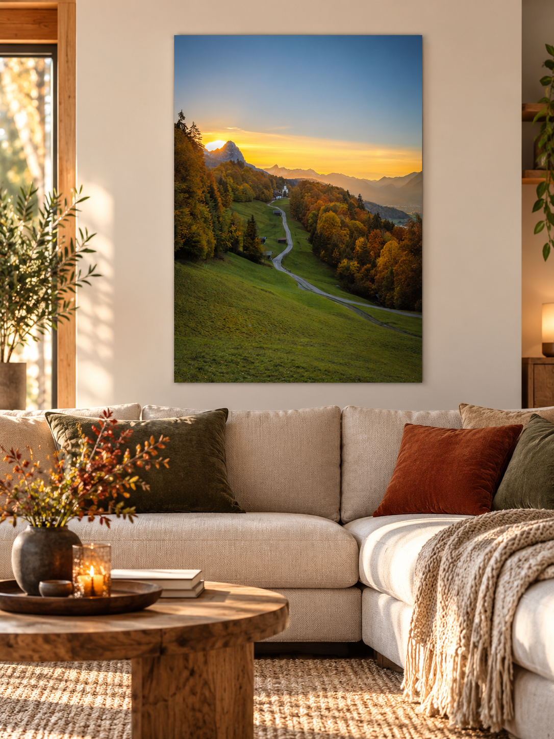 Gemütliches Wohnzimmer mit beigem Sofa, Holzmöbeln und warmen Naturtönen. An der hellen Wand hängt ein ungerahmtes, vertikales Poster mit einem herbstlichen Sonnenuntergang im Werdenfelserland. Ein geschwungener Weg führt durch bunte Wälder nach Wamberg, im Hintergrund leuchten die Berggipfel im goldenen Abendlicht.