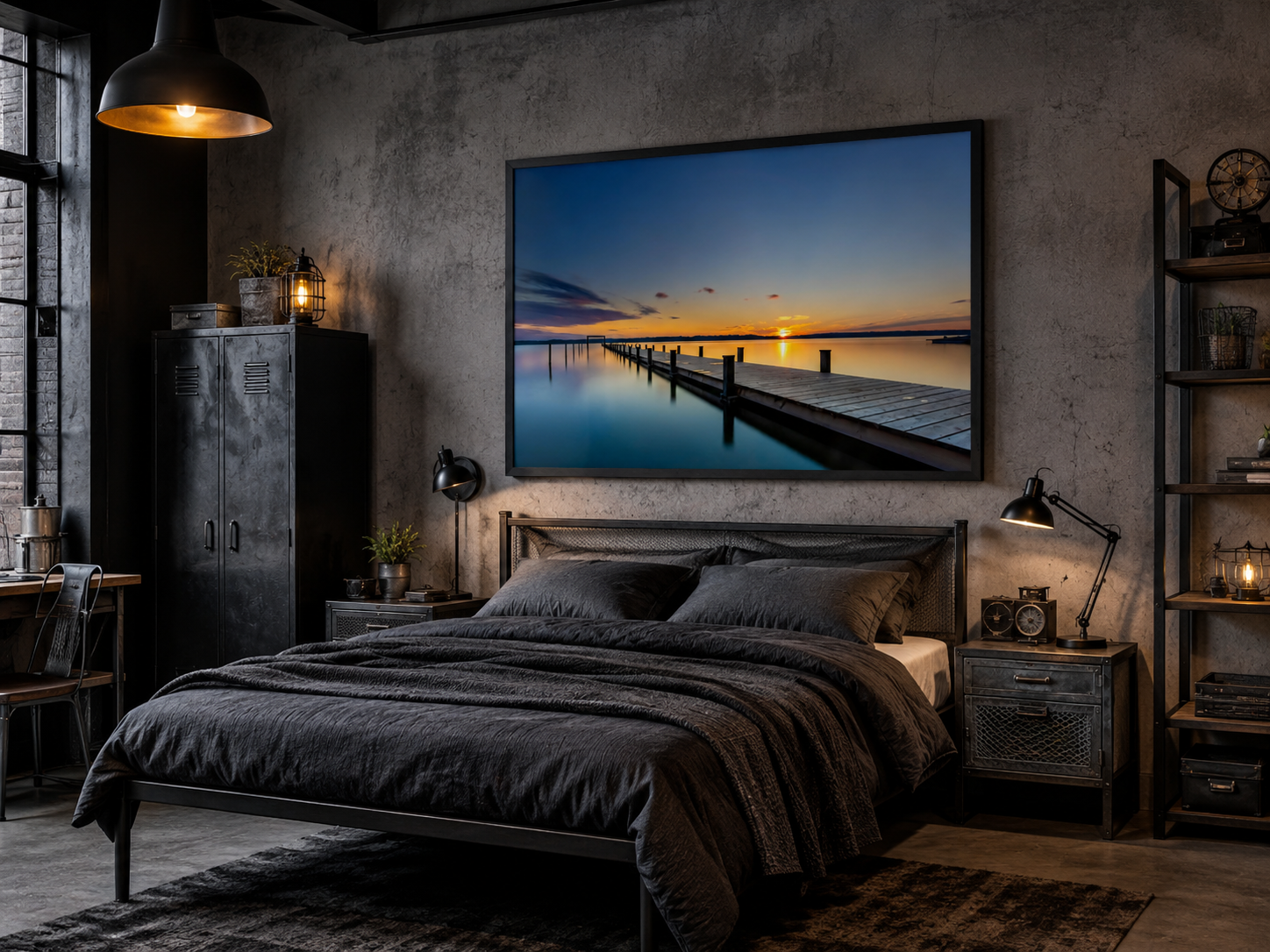 Modernes Industrie-Schlafzimmer mit Betonoptik, schwarzen Metallmöbeln und markanten Industrieelementen. Über dem Bett hängt ein großes Poster im Format 60 × 90 cm mit schwarzem Holzrahmen. Das Motiv zeigt einen langen Holzsteg, der bei Sonnenuntergang in einen ruhigen See hinausführt. Warme Goldtöne am Horizont treffen auf tiefblaue Wasser- und Himmelsfarben und schaffen einen eindrucksvollen Kontrast zur dunklen, urbanen Einrichtung. Metallregale, Industrielampen und ein Bettgestell aus schwarzem Stahl 