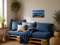 Kleine gemütliche Leseecke mit Palettensessel, blauen Kissen und passender Decke. An der hellen Wand hängt das ungerahmte Poster „Hopfensee“ im Format 30 × 45 cm horizontal. Natürliches Tageslicht und Holzelemente schaffen eine entspannte Wohnatmosphäre.