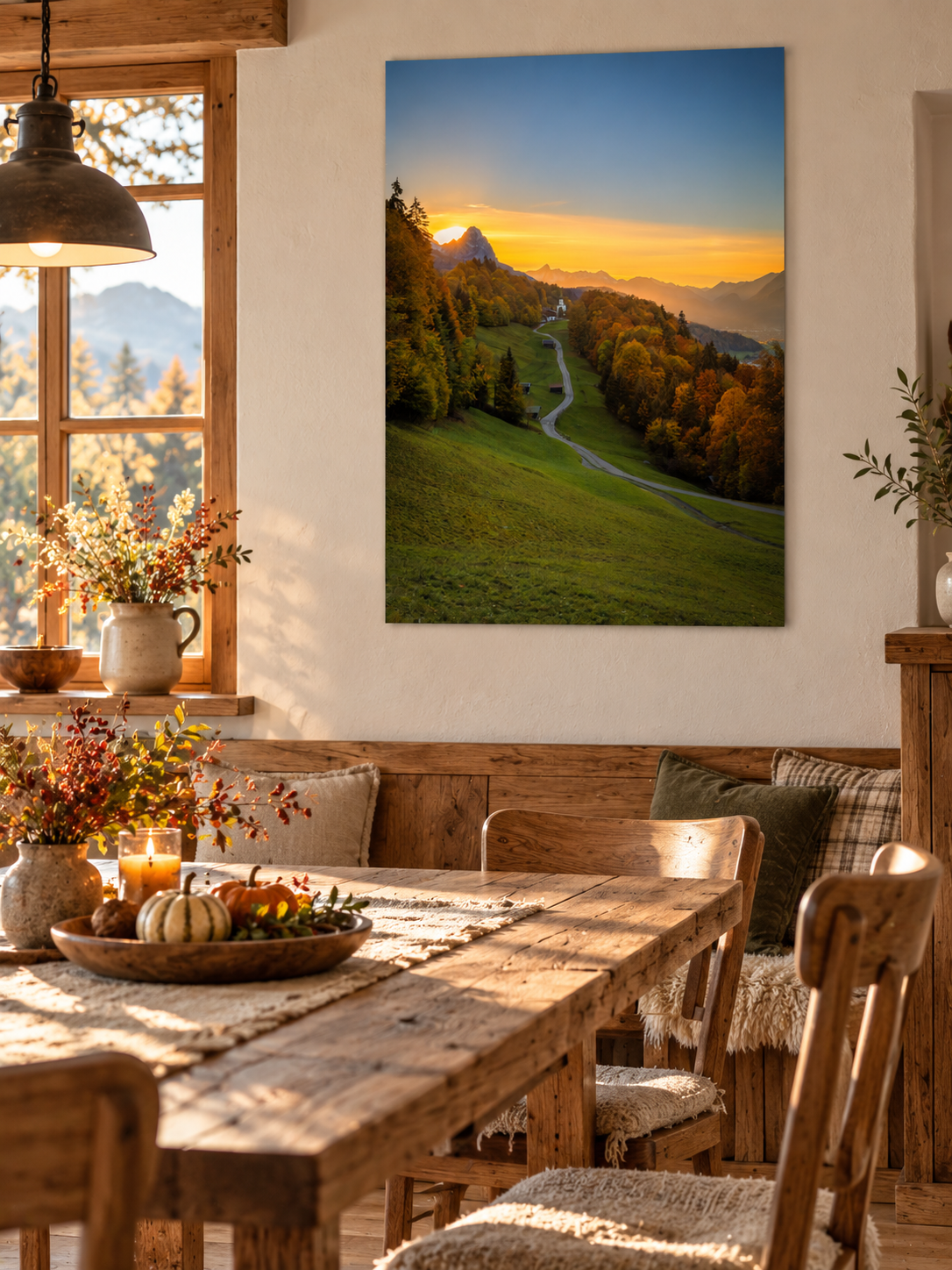 Ländliches Esszimmer mit rustikalem Holztisch, gemütlicher Eckbank und herbstlicher Dekoration. An der hellen Wand hängt ein großes, vertikales Poster ohne Rahmen. Das Landschaftsfoto zeigt den Sonnenuntergang über dem Werdenfelserland mit dem geschwungenen Weg nach Wamberg, bunten Herbstwäldern, einer kleinen Kirche und den Berggipfeln im warmen Abendlicht. Das natürliche Wandbild fügt sich harmonisch in die gemütliche Einrichtung ein.