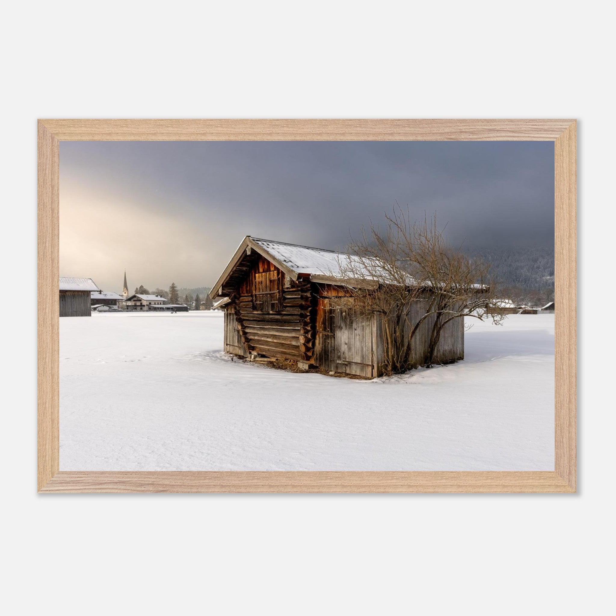 Horizontales Poster mit naturfarbenem Holzrahmen. Das Motiv zeigt eine alte, verwitterte Holzhütte auf einer verschneiten Winterwiese. Im Hintergrund sind weitere Gebäude und ein Kirchturm zu sehen, während dunkle Wolken über der winterlichen Landschaft liegen. Ein heller Lichtstrahl durchbricht die Wolkendecke und verleiht der Szene eine ruhige, stimmungsvolle Atmosphäre. Der natürliche Holzrahmen unterstreicht den rustikalen Charakter des Wintermotivs.