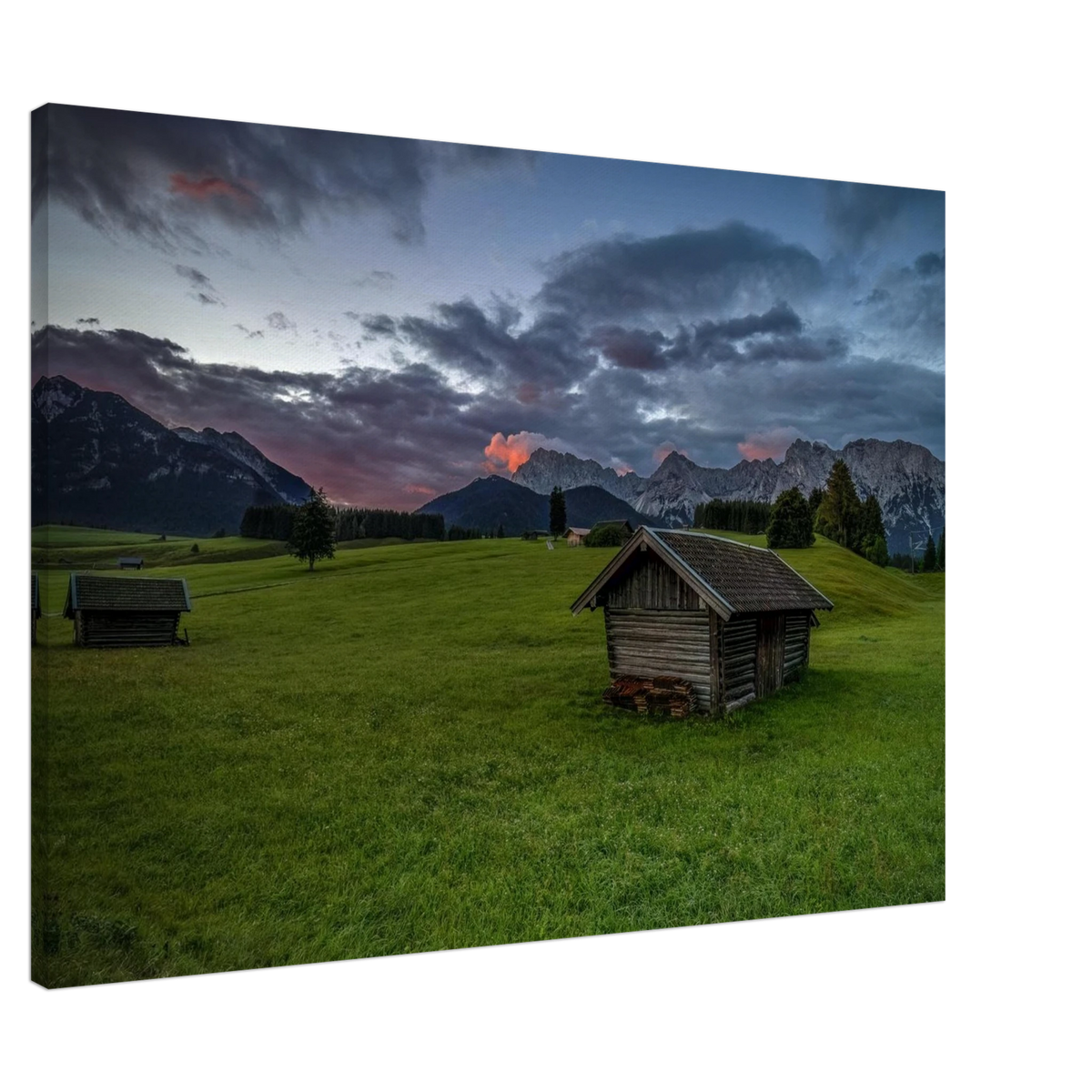 Grüne Buckelwiesen bei Krün mit traditionellen Heustadeln, dem Karwendelgebirge im Hintergrund und dramatischen Regenwolken in der frühen Morgenstimmung.
