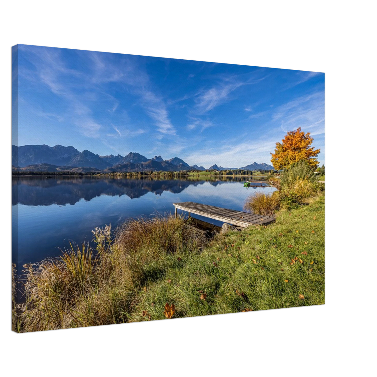 Ein goldener Herbsttag im Allgäu. Der Hopfensee liegt still vor der beeindruckenden Kulisse der Berge, das klare Wasser trägt ihre Spiegelungen und am Ufer leuchtet der Herbst in warmen Farben. Der kleine Holzsteg führt hinaus in diese besondere Ruhe, die man manchmal nur in der Natur findet.Leinwandbild