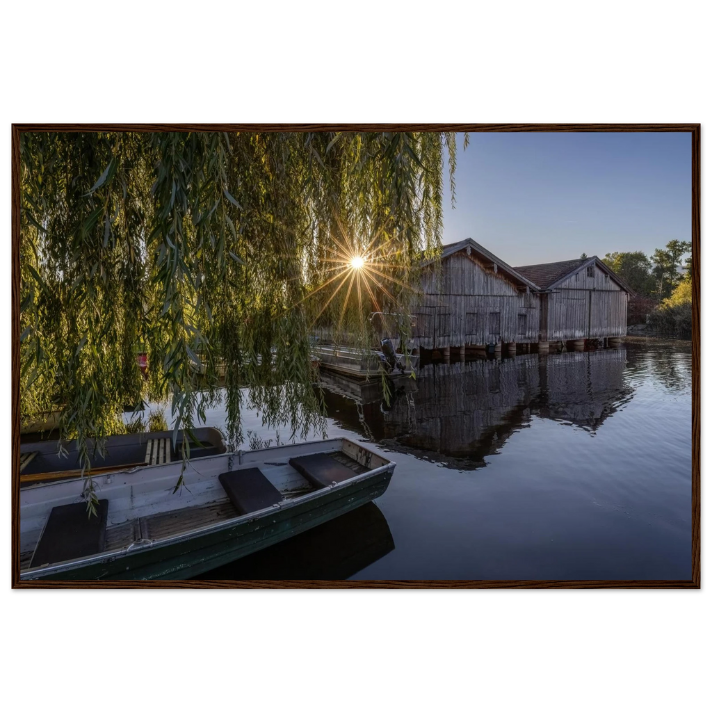 Gerahmtes Premium-Matt-Poster mit Bootshäusern in Seehausen am Staffelsee bei warmer Morgensonne, eingefasst in einen dunkelbraunen Holzrahmen.