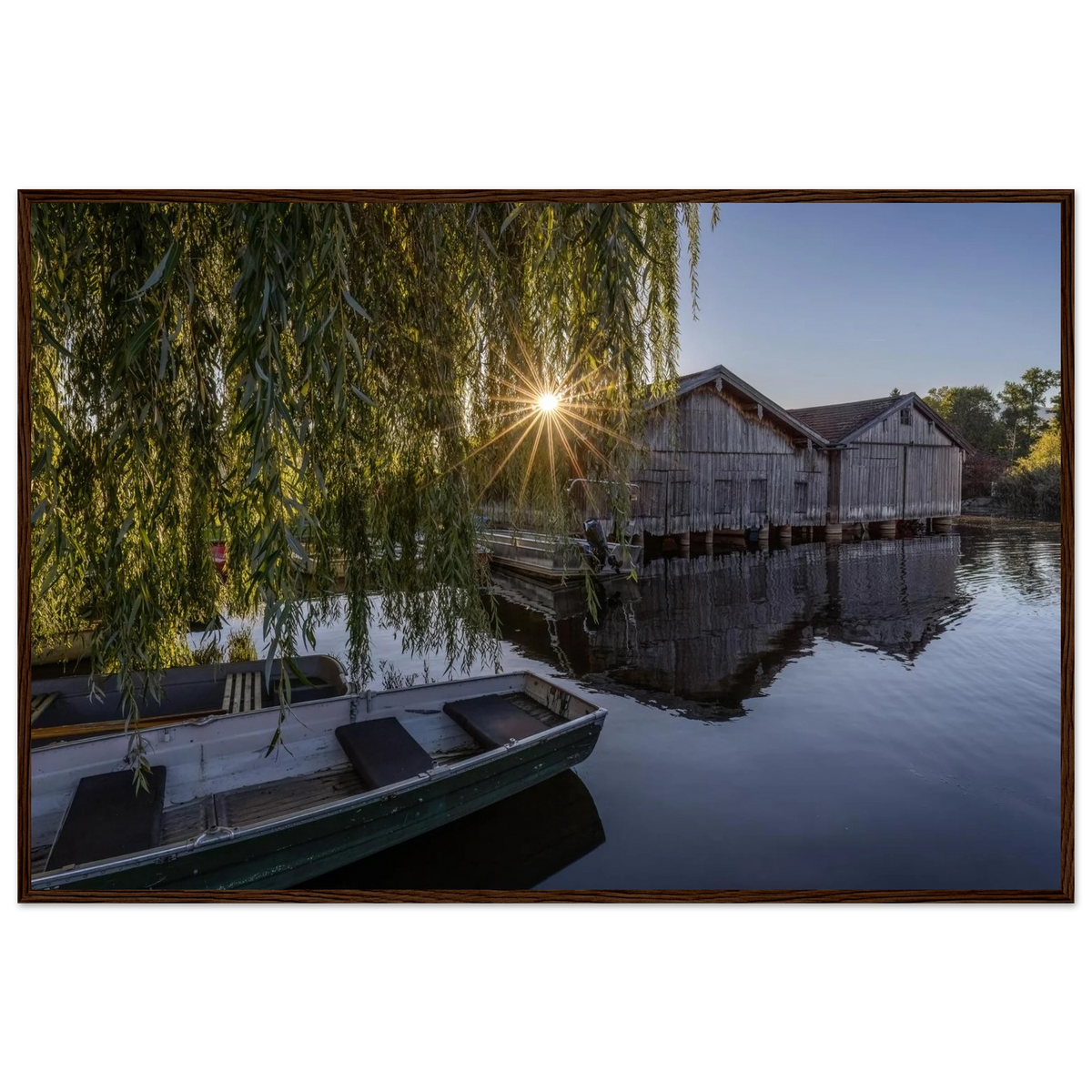 Gerahmtes Premium-Matt-Poster mit Bootshäusern in Seehausen am Staffelsee bei warmer Morgensonne, eingefasst in einen dunkelbraunen Holzrahmen.
