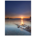Sommerlicher Sonnenuntergang am Staffelsee in Oberbayern. Die tief stehende Sonne berührt den Horizont und spiegelt sich als goldener Lichtstreifen auf dem ruhigen, durch Langzeitbelichtung weich wirkenden Wasser. Im Vordergrund ragen strukturierte Felsen ins klare Uferwasser, rechts ist eine kleine Kapelle auf einer Landzunge zu sehen. Der Himmel leuchtet in warmen Orange- und kühlen Blautönen und vermittelt eine friedliche Abendstimmung.