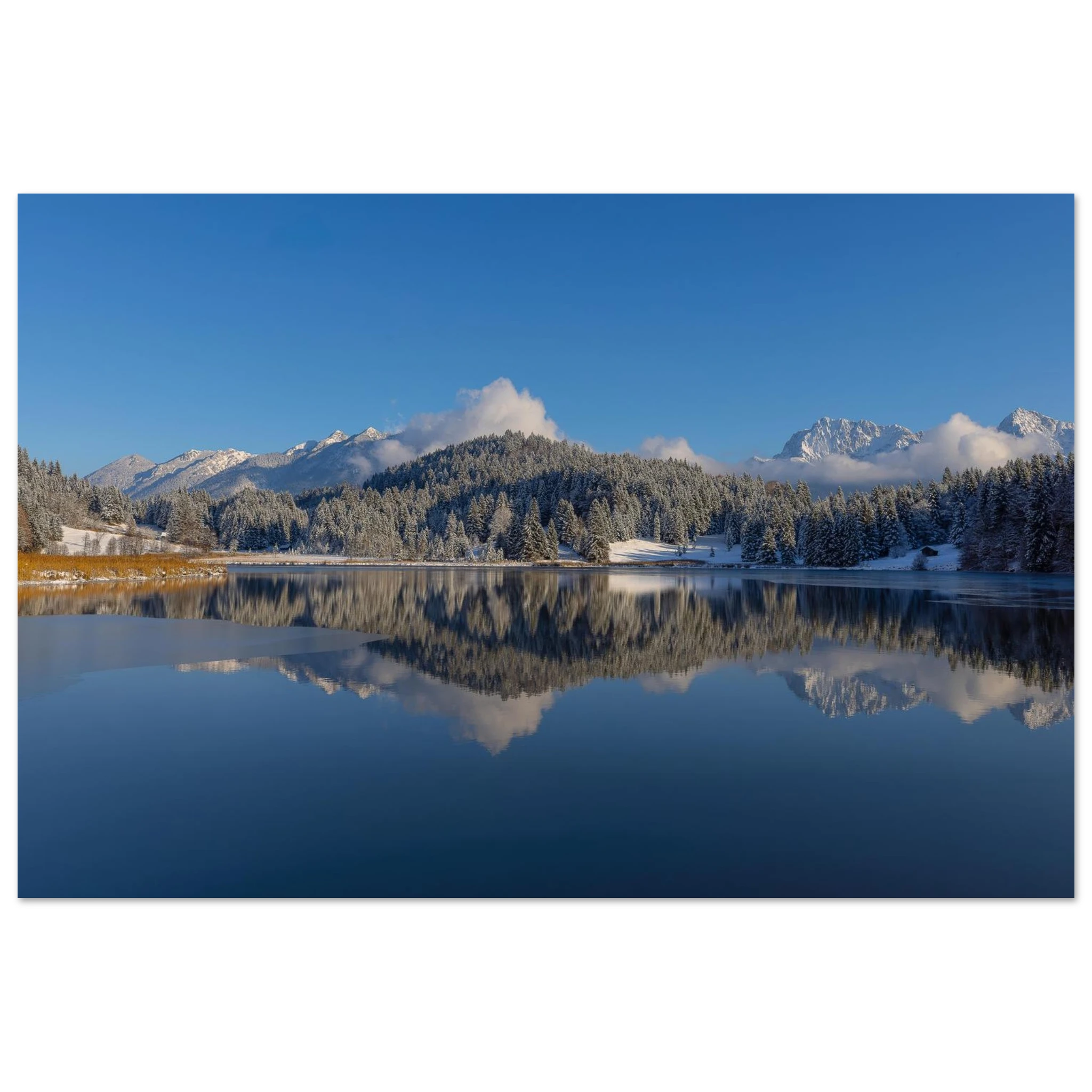 Winterlicher Geroldsee in Bayern mit spiegelglattem Wasser, verschneiten Wäldern und den Bergen des Karwendels im warmen Morgenlicht. Die klare Spiegelung im ruhigen See und der strahlend blaue Himmel verleihen der Landschaft eine stille, friedliche Atmosphäre.