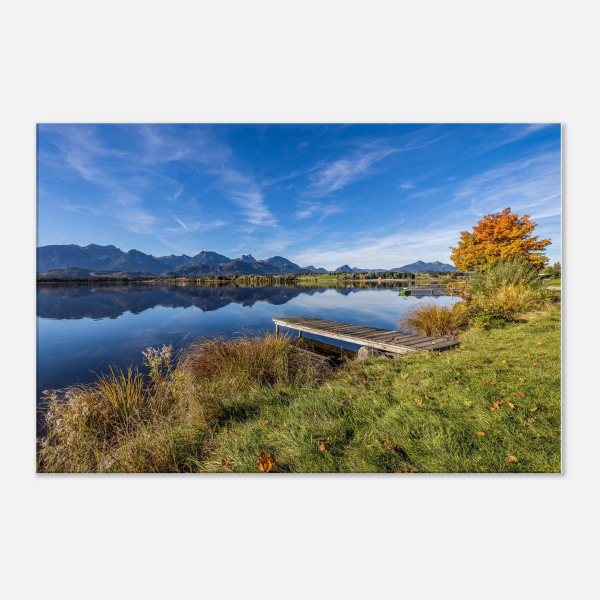 Ein goldener Herbsttag im Allgäu. Der Hopfensee liegt still vor der beeindruckenden Kulisse der Berge, das klare Wasser trägt ihre Spiegelungen und am Ufer leuchtet der Herbst in warmen Farben. Der kleine Holzsteg führt hinaus in diese besondere Ruhe, die man manchmal nur in der Natur findet.