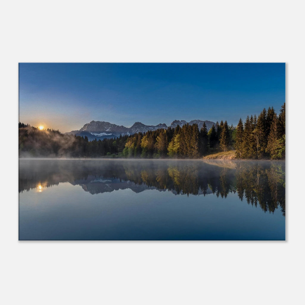 Ein stiller Morgen am Geroldsee in Oberbayern. Feine Nebelschleier ziehen sanft über das ruhige Wasser, während sich die umliegenden Wälder und die Bergwelt nahezu vollkommen im See spiegeln. Das erste warme Licht des Tages berührt die Bäume und schenkt der Landschaft eine besondere Ruhe und Tiefe.
