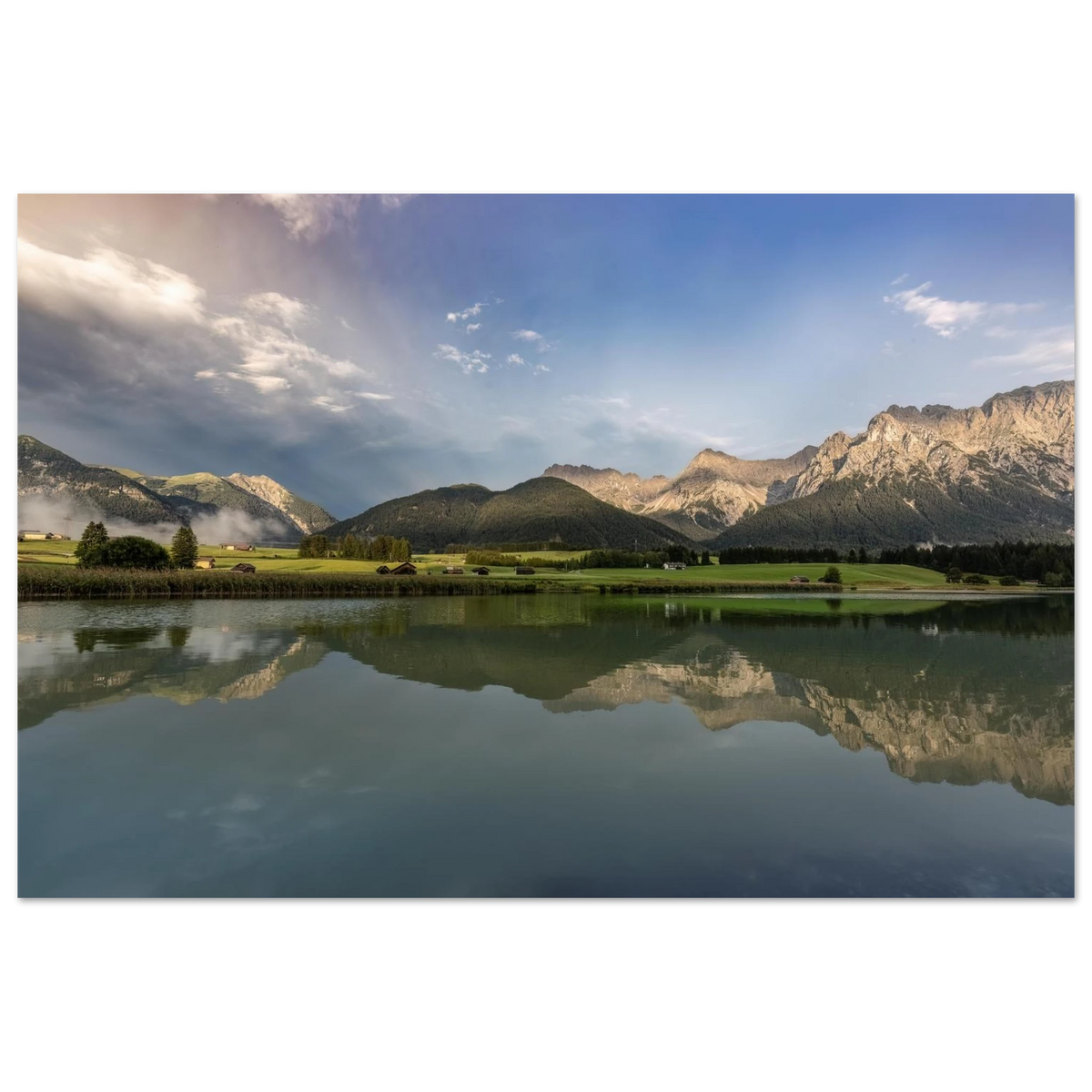 
Horizontales, ungerahmtes Poster mit Landschaftsmotiv: ruhiger Bergsee mit klarer Spiegelung, grüne Wiesen, kleine Hütten und das Karwendelgebirge im warmen Licht der goldenen Stunde unter einem dramatischen Himmel.
