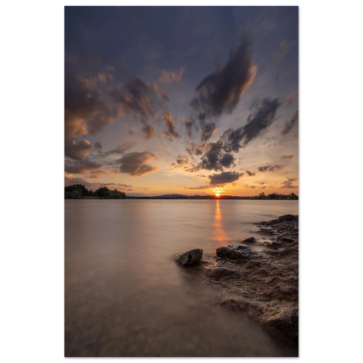 Stimmungsvolles Fotoposter mit Sonnenuntergang am See. Die tief stehende Sonne spiegelt sich im sanften Wasser, während dramatische Wolken den Himmel in warme Orange-, Rosa- und Violetttöne tauchen. Ein elegantes Wandbild mit ruhiger Abendstimmung, ideal für Wohnzimmer, Schlafzimmer und moderne Wohnräume.