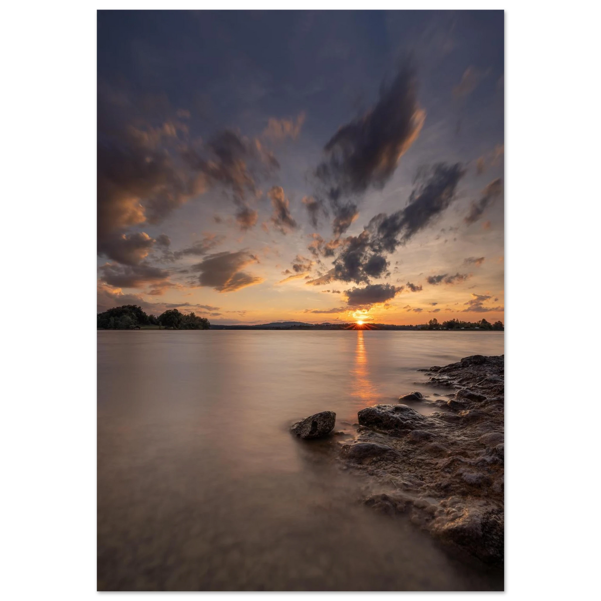Stimmungsvolles Fotoposter mit Sonnenuntergang am See. Die tief stehende Sonne spiegelt sich im sanften Wasser, während dramatische Wolken den Himmel in warme Orange-, Rosa- und Violetttöne tauchen. Ein elegantes Wandbild mit ruhiger Abendstimmung, ideal für Wohnzimmer, Schlafzimmer und moderne Wohnräume.